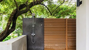 A modern outdoor shower area with a concrete wall, a wooden fence, and a tree in the background. - Casa Pipeline: Jungle Villa, Pool, Sleeps 14 (Nosara)