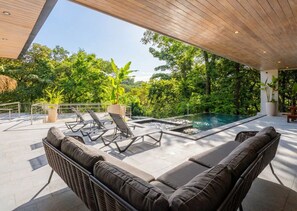 Zona de piscina al aire libre con sillones de descanso y techo de madera.