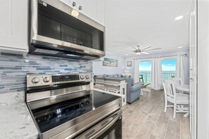 A modern kitchen with stainless steel appliances, a tiled backsplash, and a dining area with white furniture.