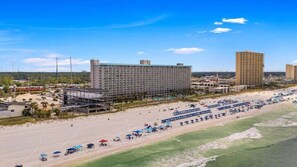 A beachfront hotel with multiple floors, a sandy beach in front, and several umbrellas.