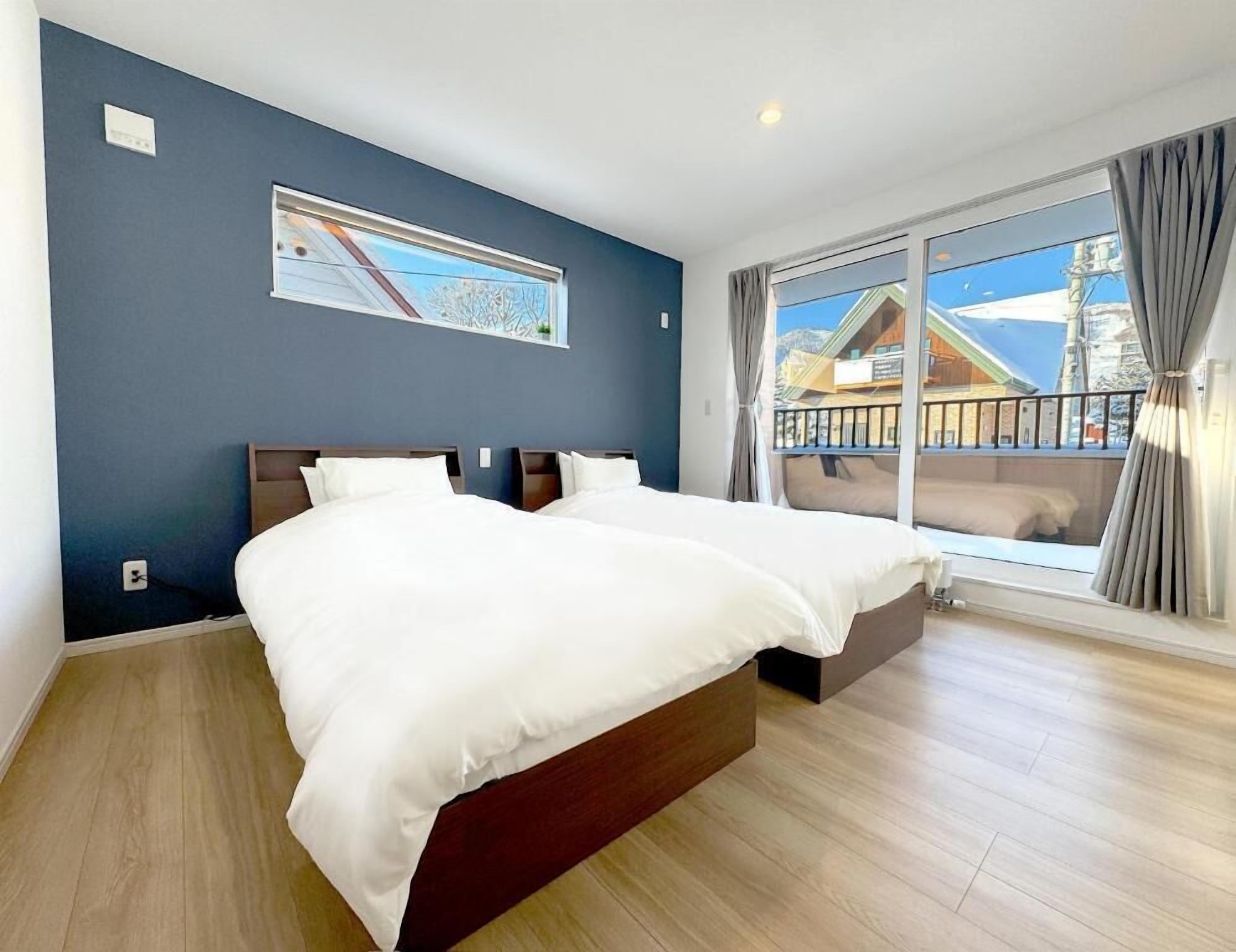 A modern hotel room with a large bed, a view of a building through a window, and a painting on the wall.