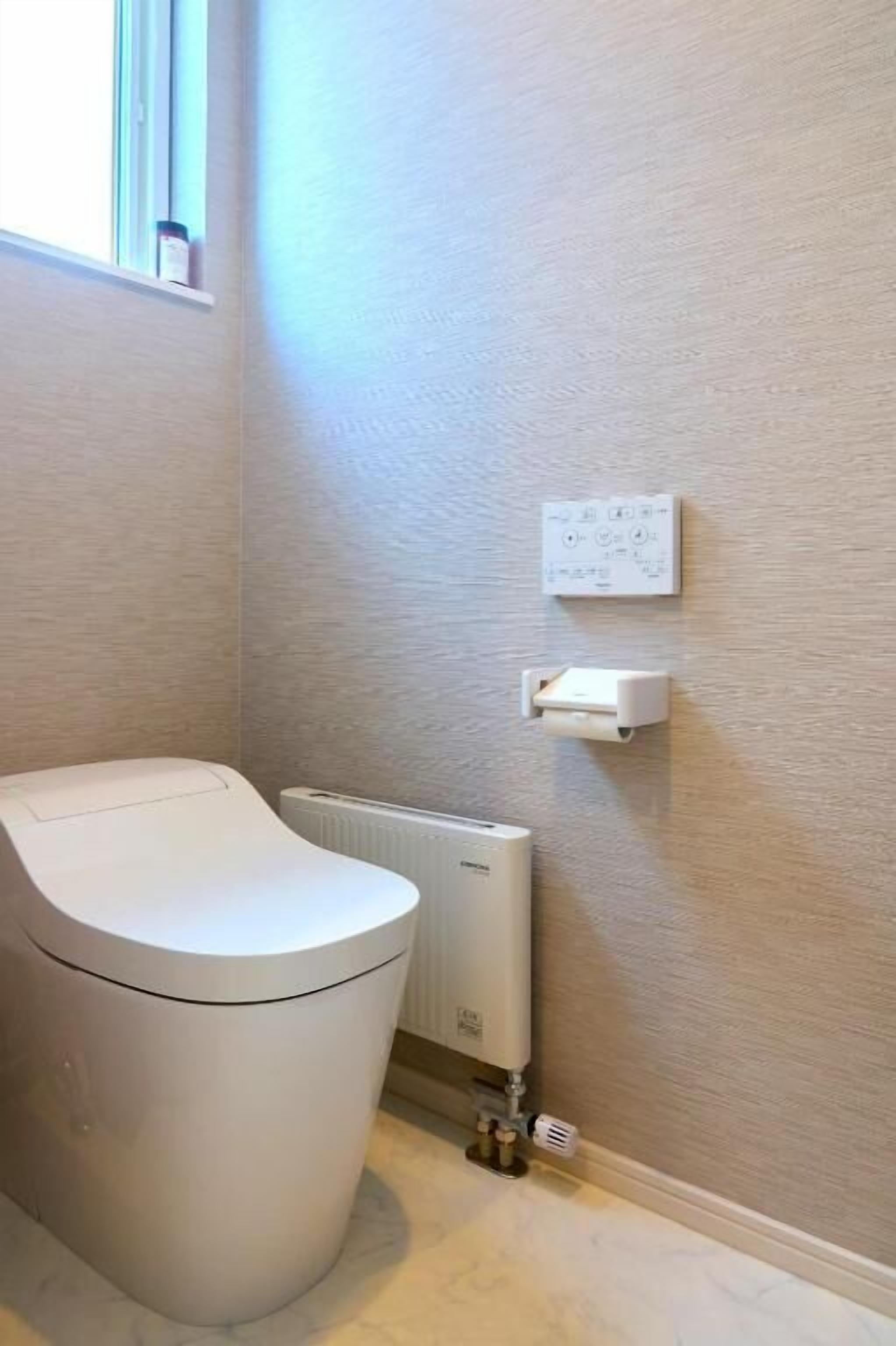 A bathroom with a toilet, a radiator, and a wall-mounted electrical outlet.