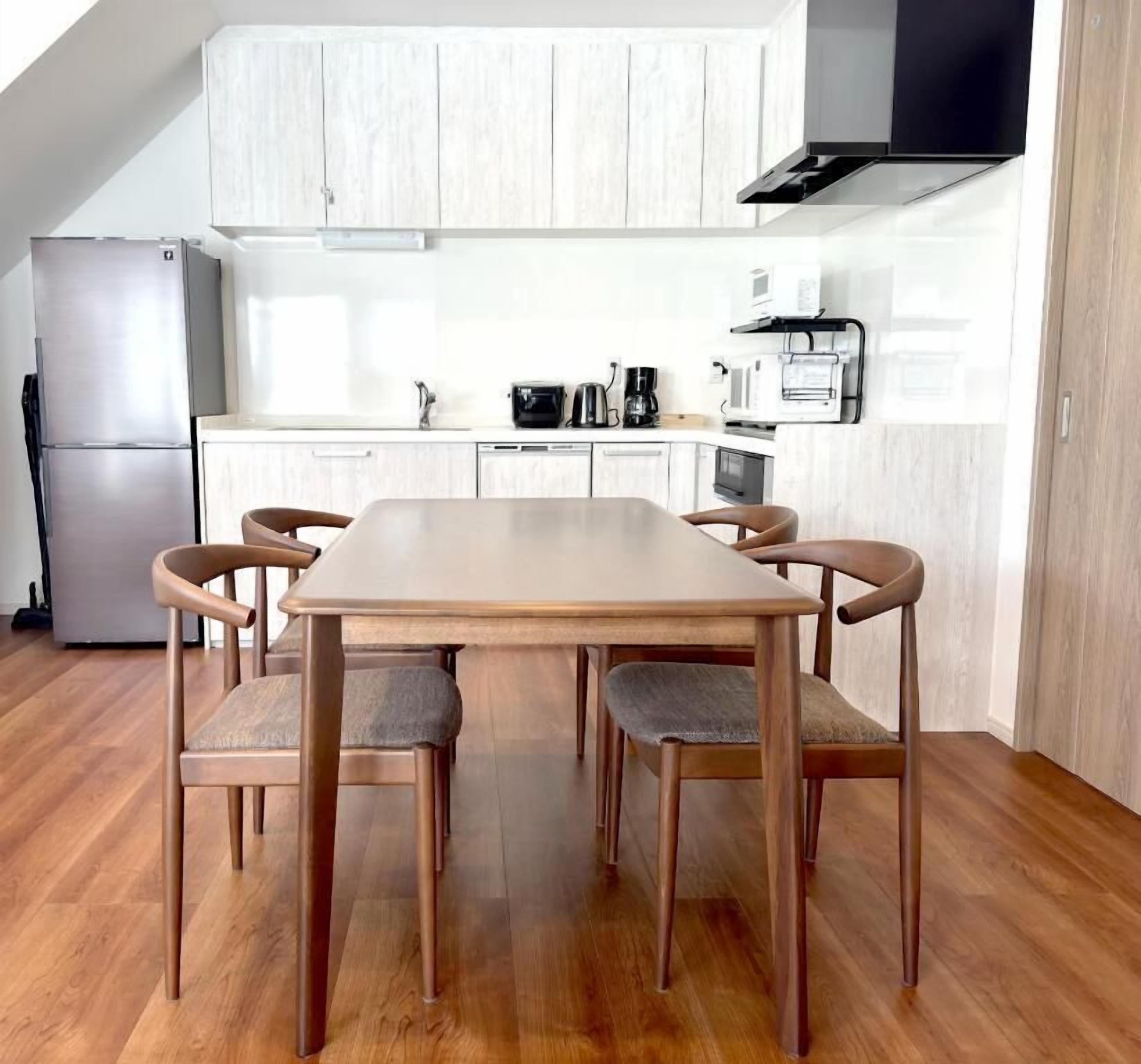 A modern kitchen with white cabinetry, a central island, and a dining area with wooden chairs.