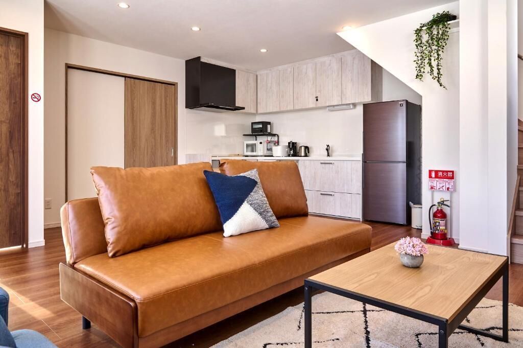 Un salon moderne avec un canapé en cuir marron, une table basse en bois et un coin cuisine à l’arrière-plan.