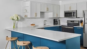 A modern kitchen with white cabinets, a blue island, stainless steel appliances, and a vase with flowers.