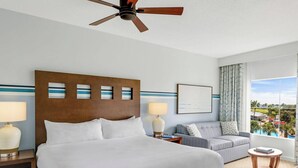 A hotel room with a large bed, a sofa, a ceiling fan, and a window with a view.