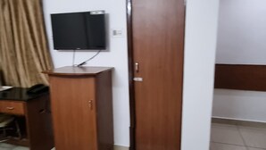 A room with a wooden door, a television mounted on the wall, a desk with a chair, and a patterned rug on the floor. - Hotel Bharath (Chennai)