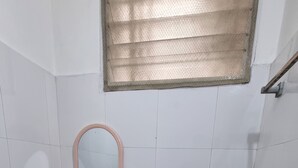 A small, tiled bathroom with a toilet, sink, and a window above the sink. - Hotel Bharath (Chennai)