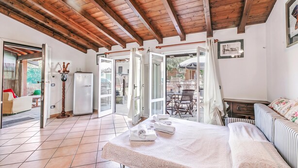 A room with a bed, a table with towels, a refrigerator, and a door leading to an outdoor area. - Casa Rolè (Dormelletto)
