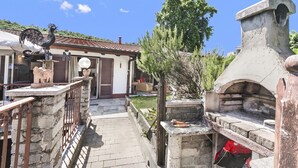 A courtyard with a stone oven, a rooster sculpture, and a house with a tiled roof. - Casa Rolè (Dormelletto)