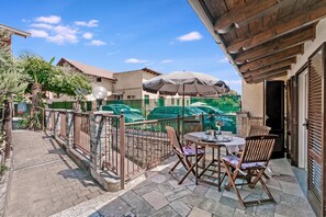 Un patio al aire libre con una mesa, sillas, una sombrilla y vista a una piscina.