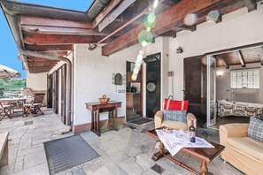 An outdoor patio area with a wooden pergola, a dining table with chairs, and a sofa.
