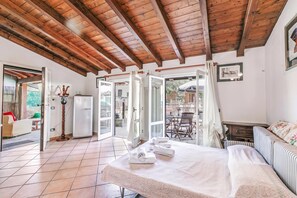 Una habitación con una cama, una mesa con toallas, un refrigerador y una puerta que da a un espacio exterior.