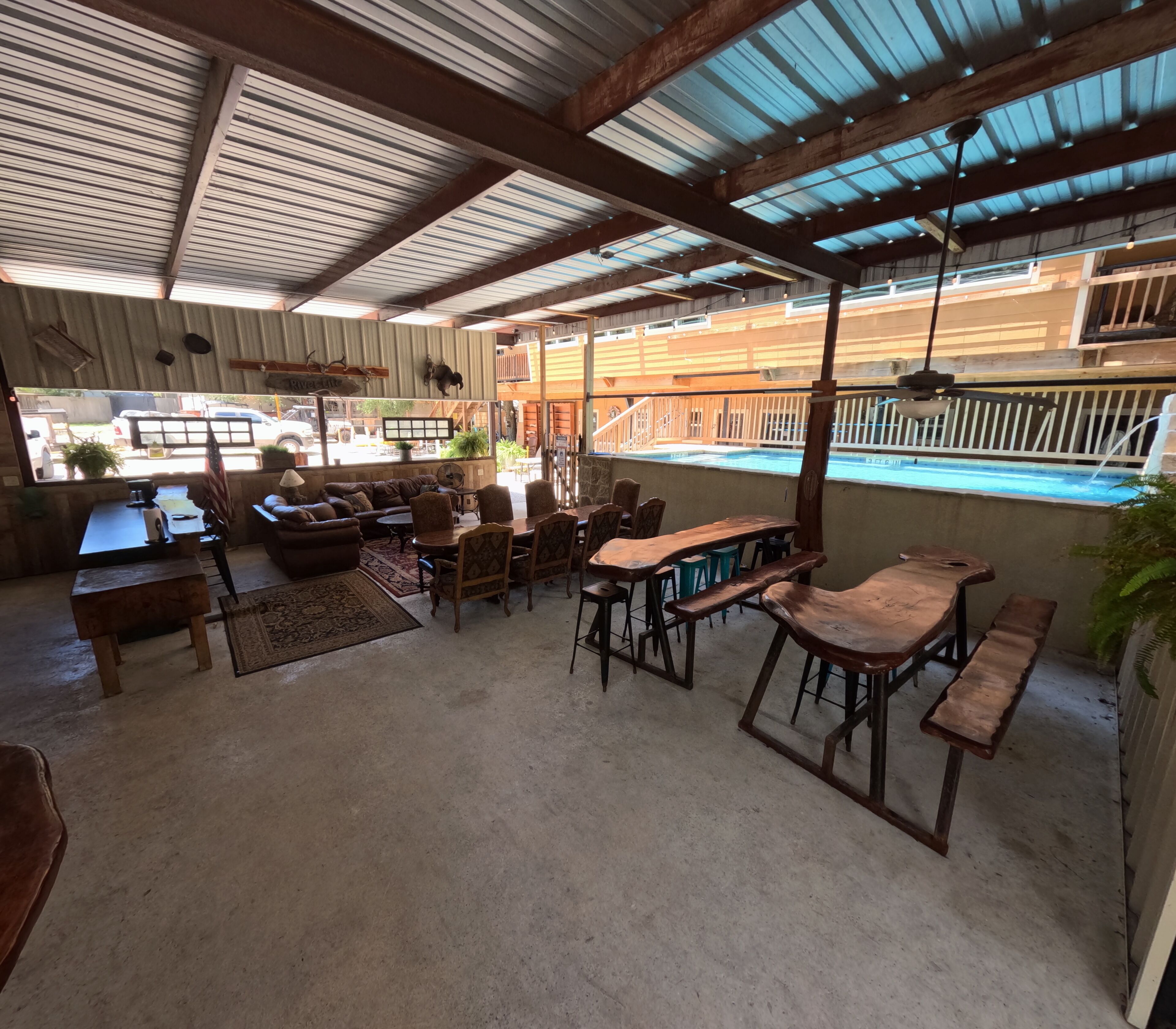 Un espacio de sala-comedor abierto con vista a la piscina, con una combinación de muebles de madera y piso de concreto.