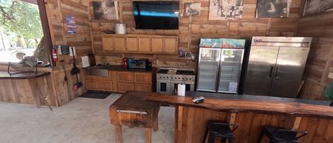 A rustic kitchen with wooden cabinets, a gas stove, a refrigerator, and a bar area with stools.