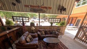 A covered outdoor seating area with leather sofas, a round table, and a patterned rug. - Avie's Hideaway, Exclusive Private Riverfront @Vacation Frio River Room #1 (Concan)