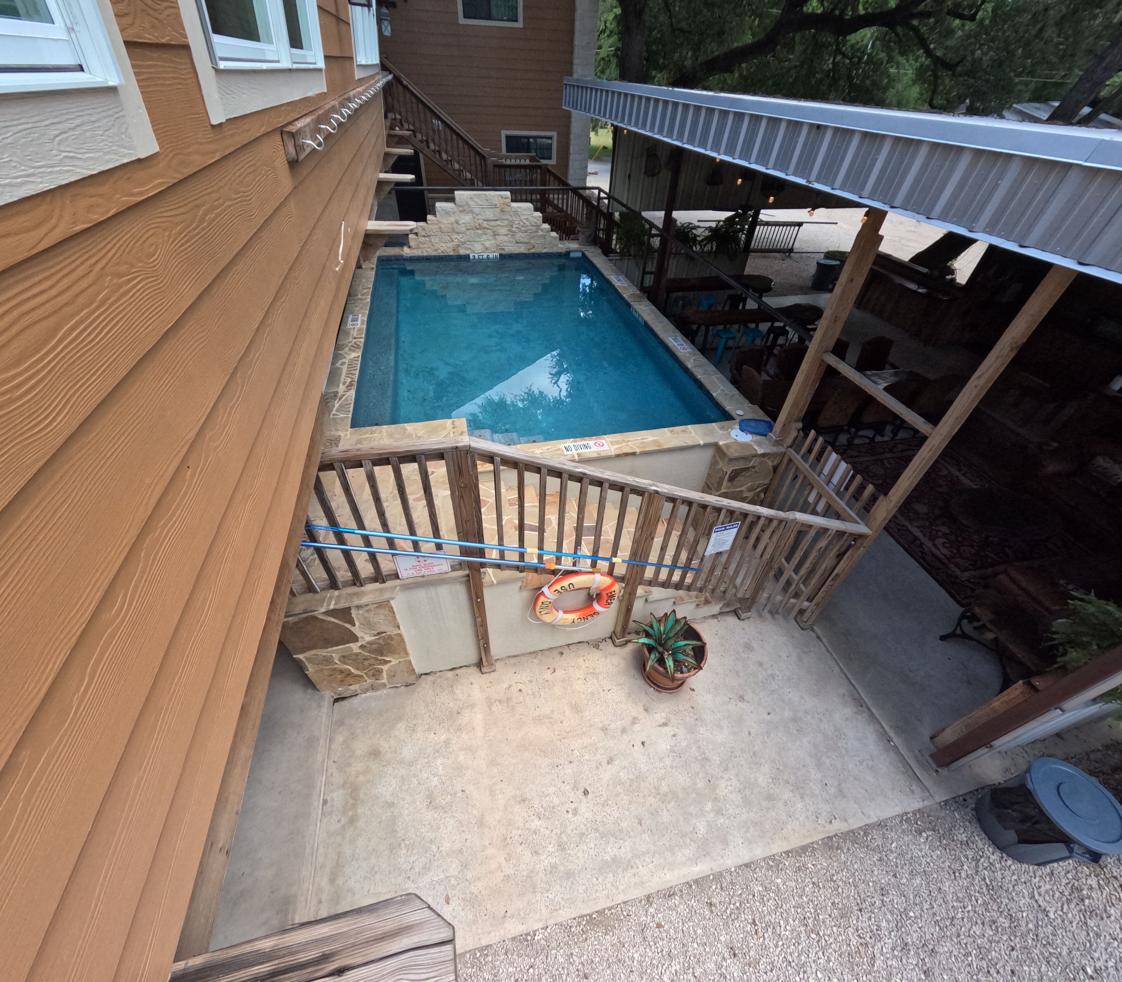 A backyard with a swimming pool, wooden deck, and a covered patio area.