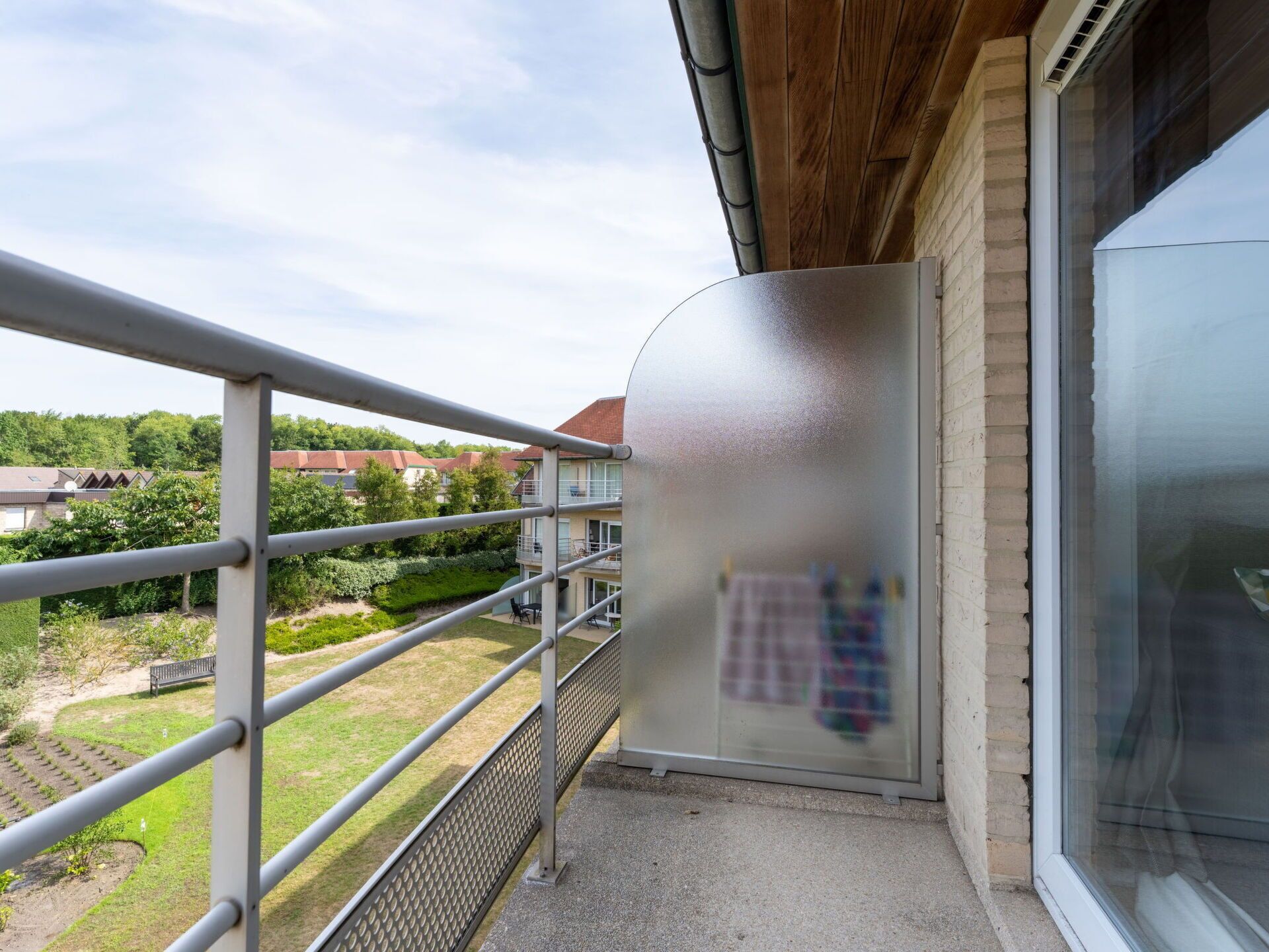 Een balkon met een metalen hekwerk, met uitzicht op een tuin en omliggende huizen.