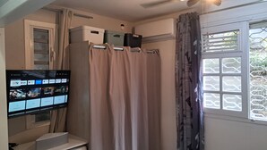 Ein Zimmer mit einem wandmontierten Flachbildfernseher, einem Fenster mit gemustertem Vorhang und einem Deckenventilator.