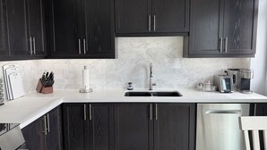 A modern kitchen with dark wood cabinets, a white marble backsplash, stainless steel appliances, and a built-in dishwasher. - Premier Host • Lux 2BR Pickering Retreat • AC, WiFi & Free Parking (Pickering)