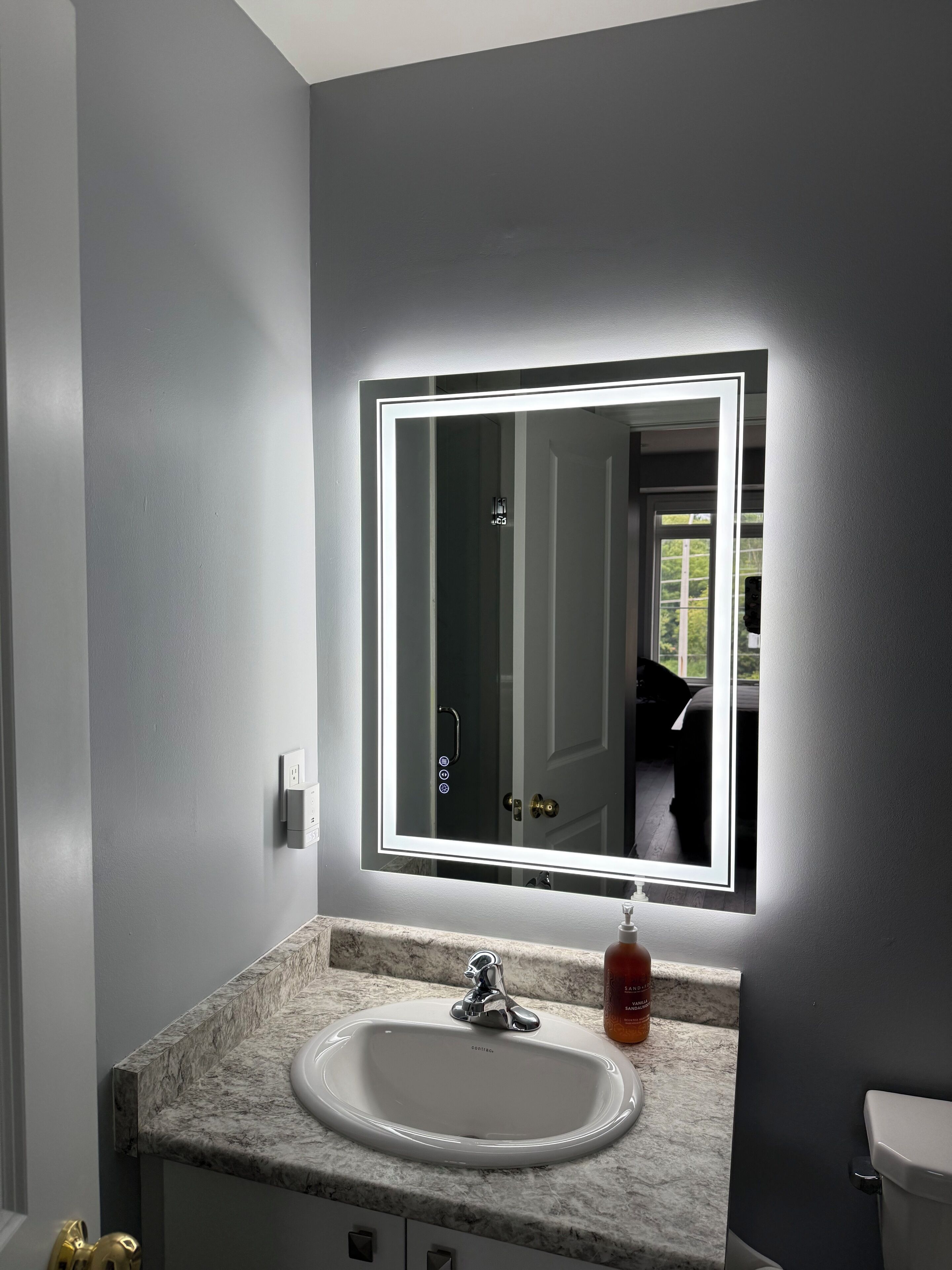 Ein Badezimmer mit Marmorwaschbecken, einem Spiegel mit integrierter Beleuchtung und einer Toilette.