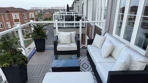 A balcony with a wicker sofa and a matching ottoman, a glass-top coffee table, and potted plants. - Premier Host • Lux 2BR Pickering Retreat • AC, WiFi & Free Parking (Pickering)