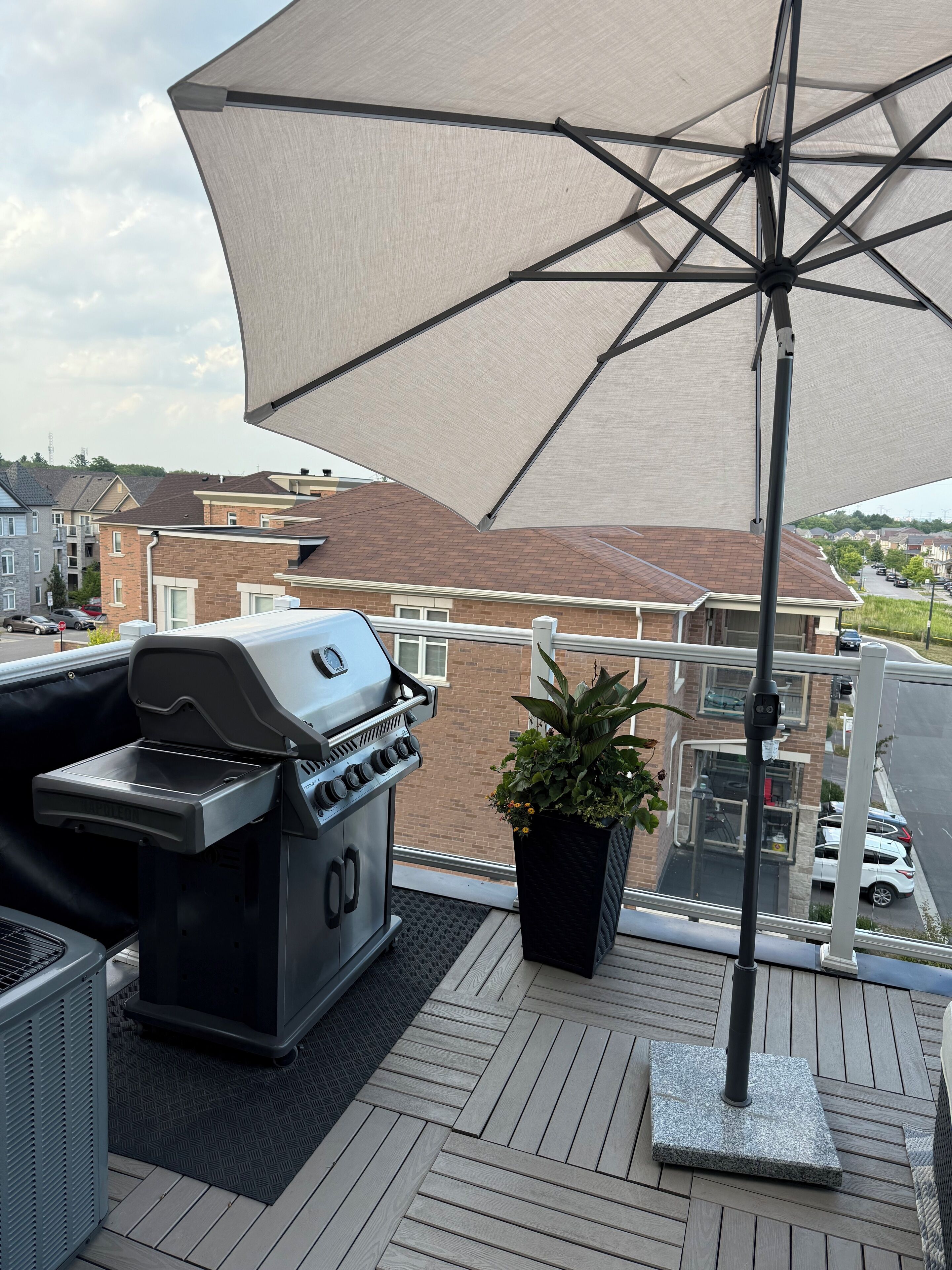A balcony with a barbecue grill, a potted plant, and a large umbrella providing shade.