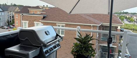 A balcony with a barbecue grill, a potted plant, and a large umbrella providing shade.