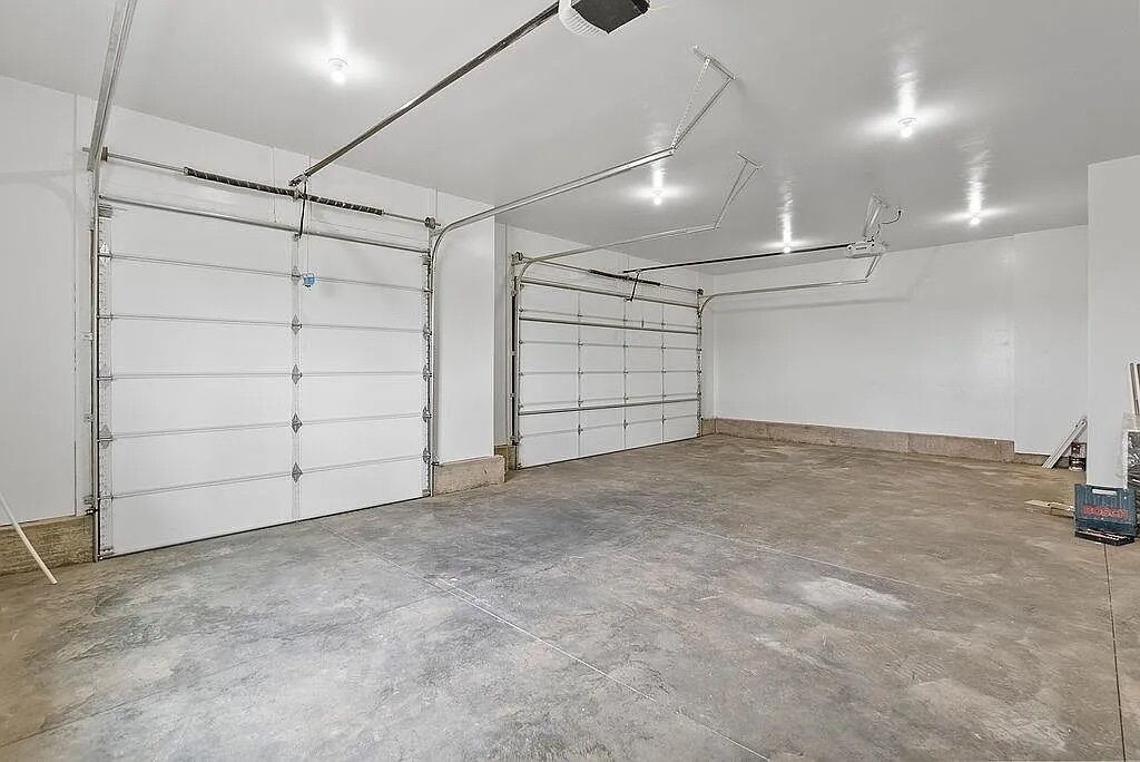 A garage with two large white garage doors, a concrete floor, and overhead lighting.