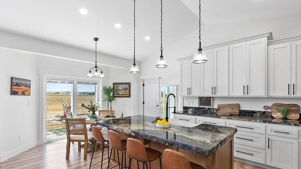 Una cocina moderna con una isla grande, armarios blancos e iluminación colgante.