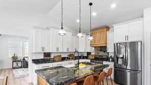Una cocina moderna con armarios blancos, un refrigerador de acero inoxidable y una isla de mármol con taburetes de bar.