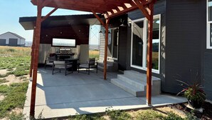 Un patio techado con una parrilla y zona de estar, una casa con ventanas amplias y vistas al paisaje circundante.