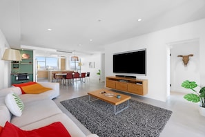 A modern living room with a sofa, coffee table, TV, and a dining area with chairs and a table.