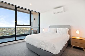A modern bedroom with a large bed, bedside lamps, and a view through a sliding glass door.