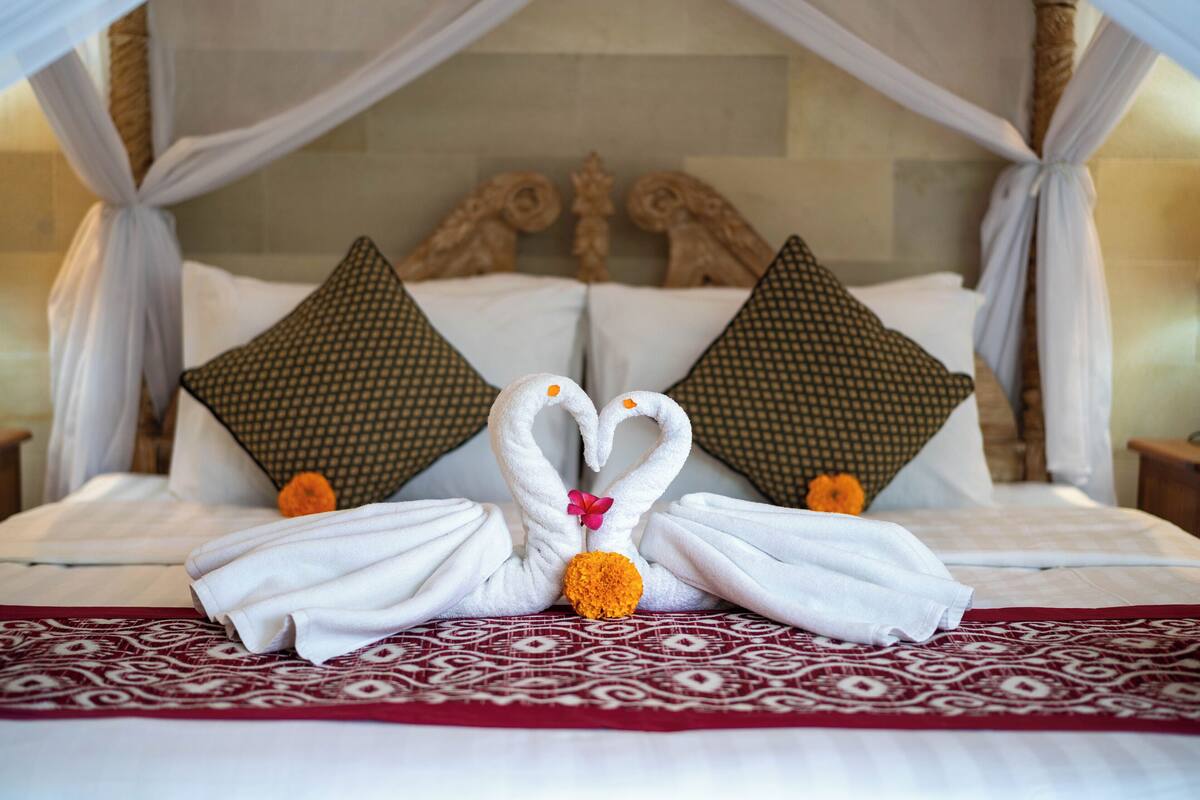 A bed with a canopy, two decorative pillows, a floral arrangement, and a patterned bedspread.