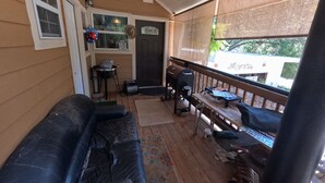 A covered porch with a black leather couch, a grill, and a small table.