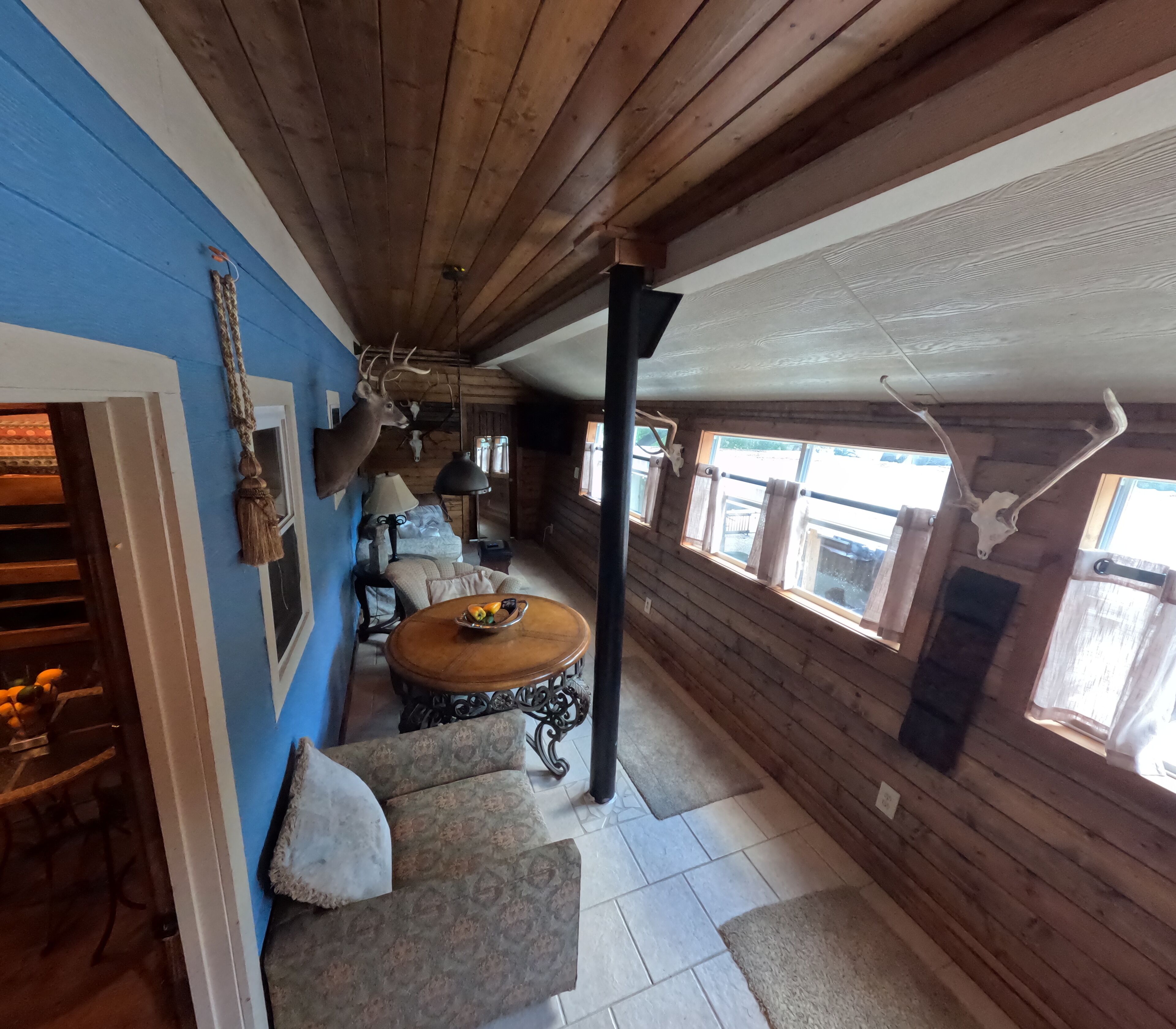 A log cabin interior with a blue wall, wooden ceiling, and a dining area with a table and chairs.