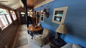 A room with a blue wall, a deer head mounted on the wall, a round table with a bowl of fruit, a chair, and a lamp. - Harper's Hideaway, #5 Exclusive Private Riverfront @Vacation Frio River (Concan)