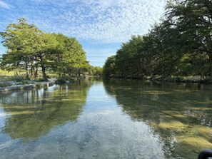 Une rivière aux eaux claires où se reflètent les arbres et le ciel, entourée d’une végétation luxuriante.