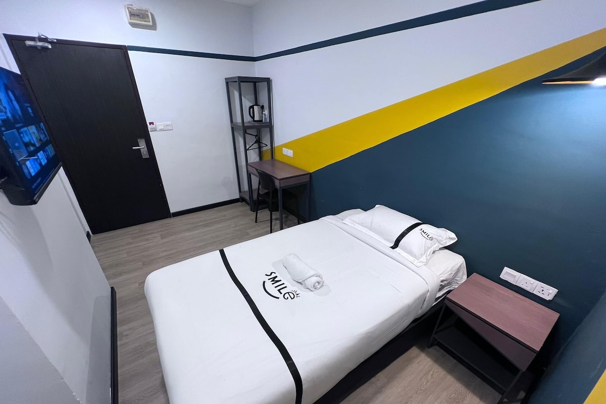 A hotel room with a bed, a desk, a chair, and a small table.