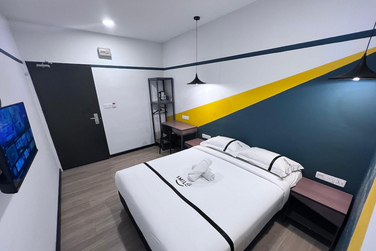A hotel room with a bed, a desk, a chair, and a TV.