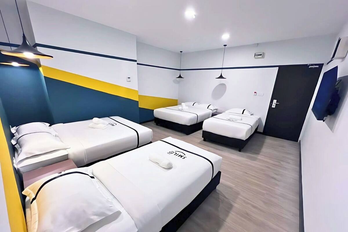 A hotel room with four beds arranged in a row, a flat-screen TV mounted on the wall, and a modern design with blue and yellow accents.