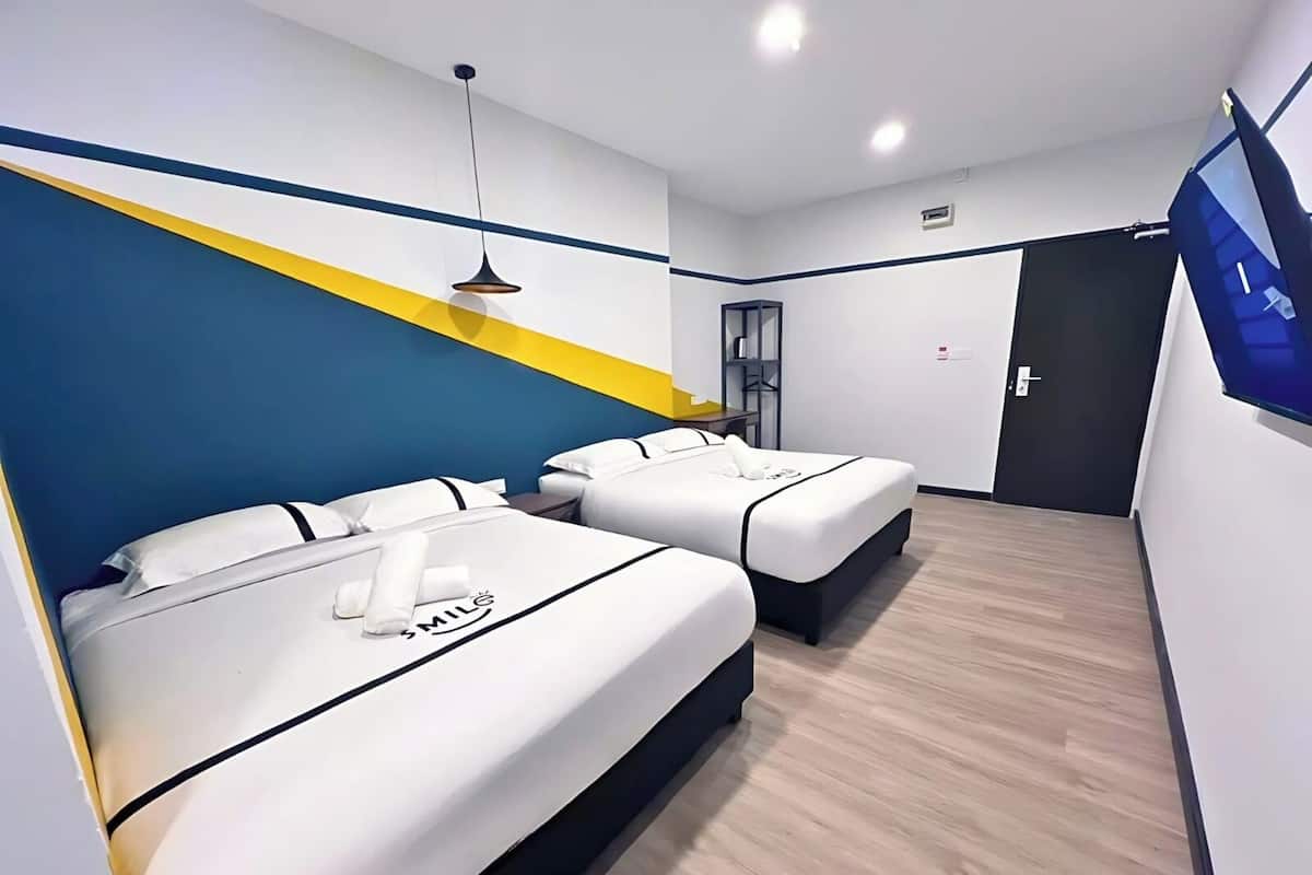 A hotel room with two beds, a TV mounted on the wall, and a wooden floor.