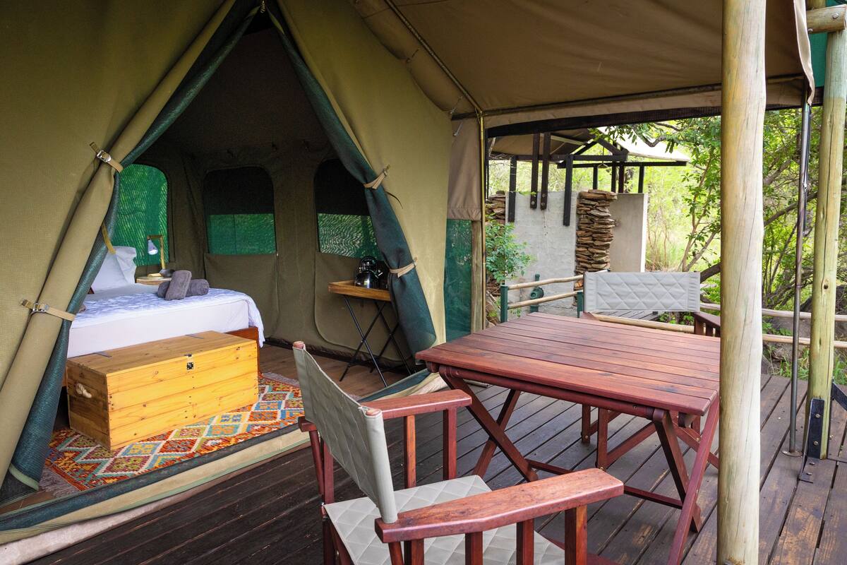 A tent with a bed, a wooden chest, and a table with chairs.