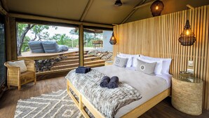 A bedroom with a large bed, wooden headboard, and a view of the outdoors. - Bushveld Bivouac Private Camp (Mica)