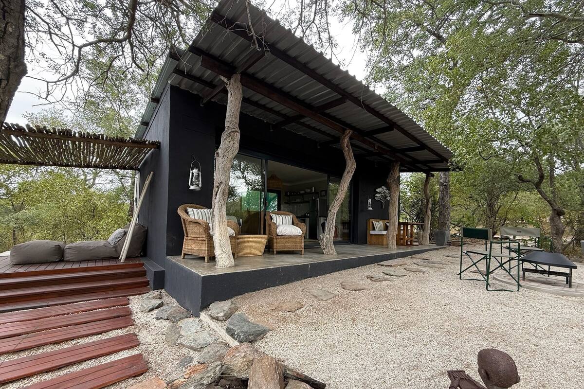 A modern outdoor living space with a covered patio, wicker furniture, and a stone pathway leading to a seating area.
