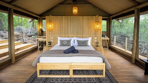 A wooden-framed bedroom with a bed, two bedside tables, a nightstand, and a large window with a view of the outdoors. - Bushveld Bivouac Private Camp (Mica)