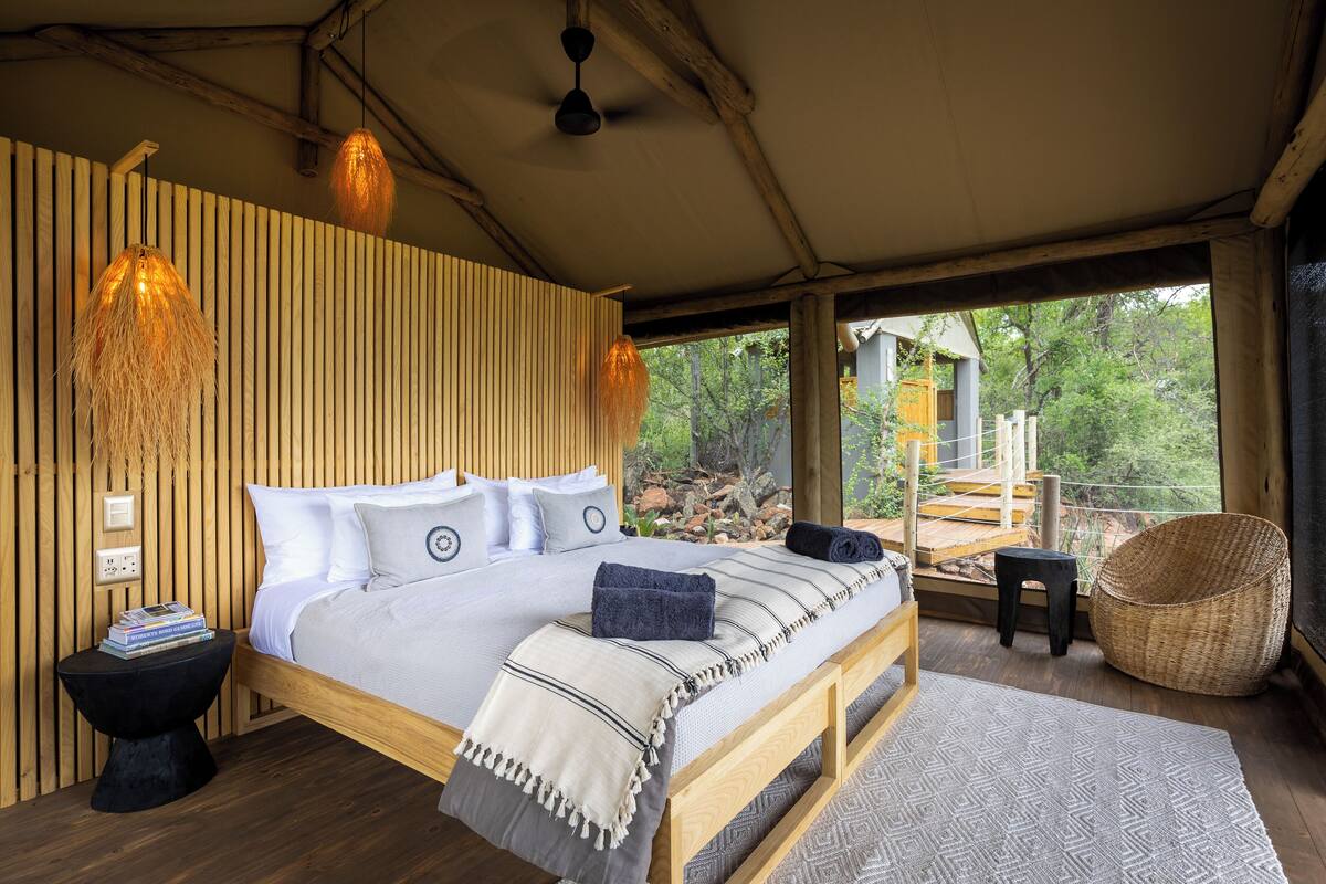 A bedroom with a wooden bed, a nightstand, a woven chair, and a view of the outdoors.