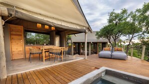 An outdoor deck with a wooden table and chairs, a hot tub, and a covered seating area with cushions. - Bushveld Bivouac Private Camp (Mica)