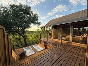 Eine Holzdielen-Terrasse mit zwei Whirlpools, einem überdachten Sitzbereich und Blick auf eine bewaldete Landschaft.